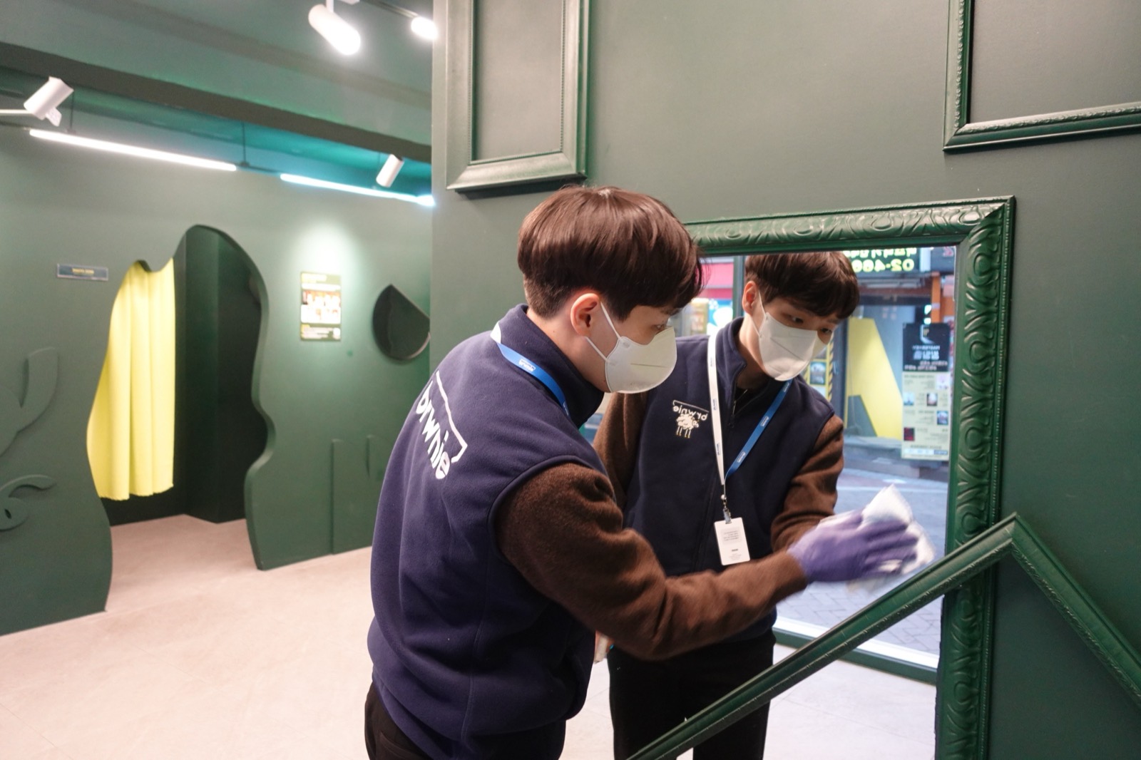 크루 두 명이 셀프사진관 거울을 닦는 모습